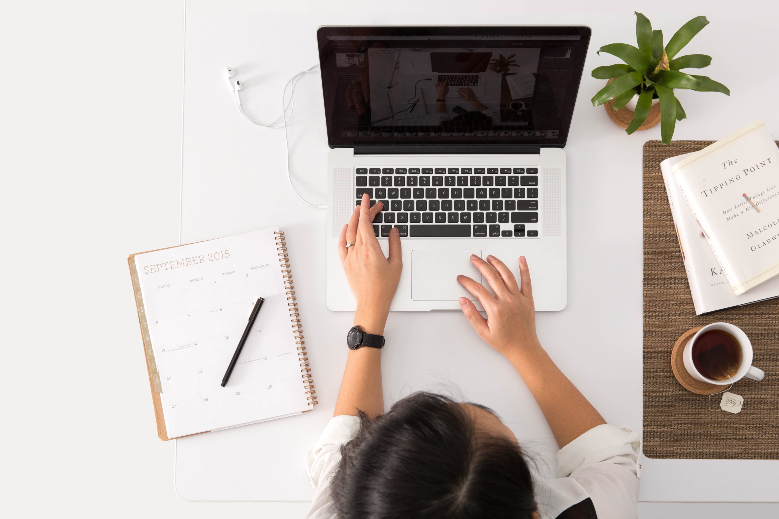 women using apple laptop on desk with coffee, diary and plant